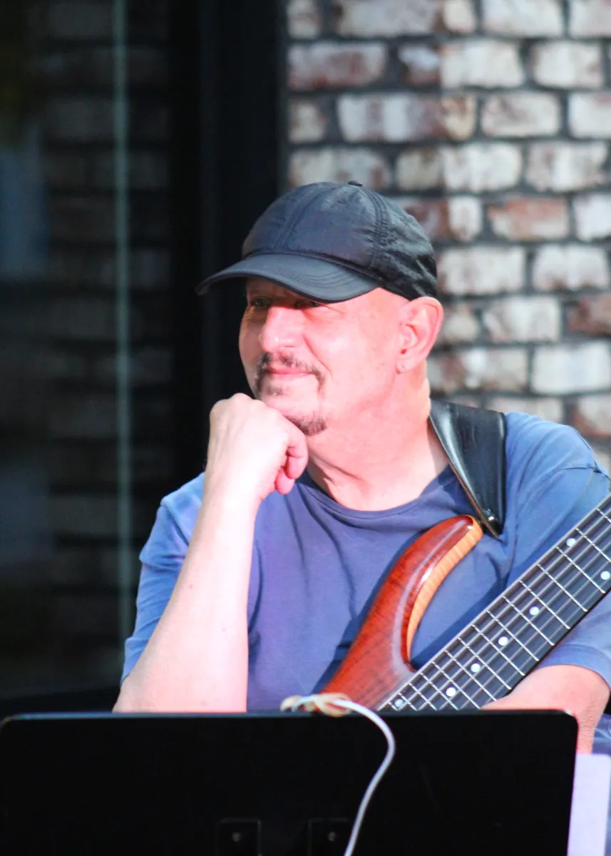 Russ Rodgers between numbers, bass in hand, against a brick wall