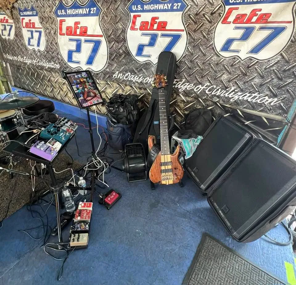 Stage corner at Cafe 27 in Florida — drums, both pedalboards, bass on a stand, iPad, and monitor speakers
