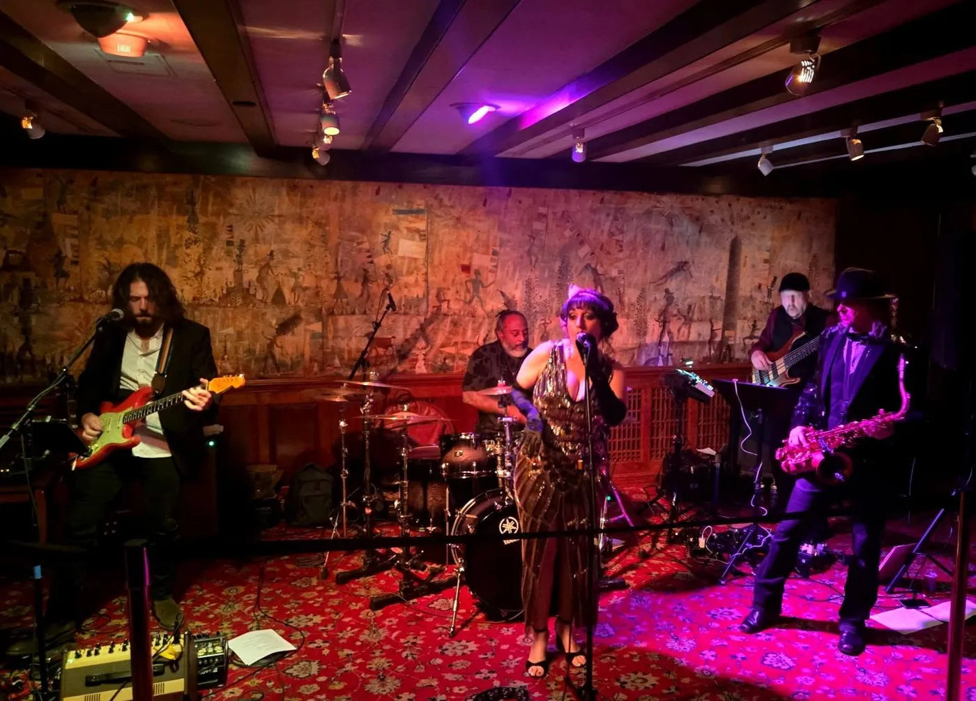 Five-piece band with vocalist and saxophone in an ornate tapestry-walled room, Russ Rodgers on bass